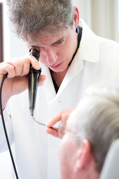 doctor in white coat peering into nasal inspection device with back of patient's head visible in the foreground