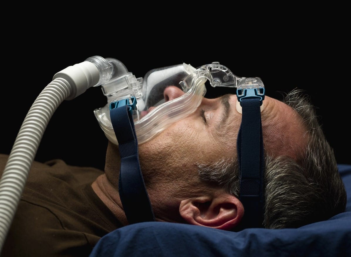 man sleeping wearing clear cpap device with tube attached on face undergoing sleep apnea treatment