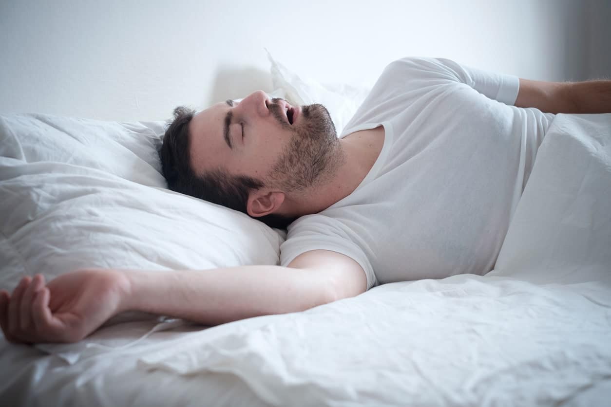 An image of a man laying in bed suffering from sleep apnea.