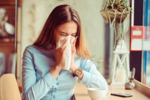 Young woman got nose allergy, flu sneezing nose sitting at the table