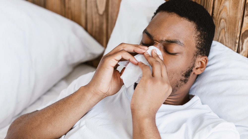 A sick man lies on the couch an blows his nose