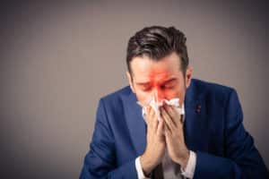 Sick businessman blowing nose in a tissue.