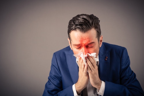Sick businessman blowing nose in a tissue.