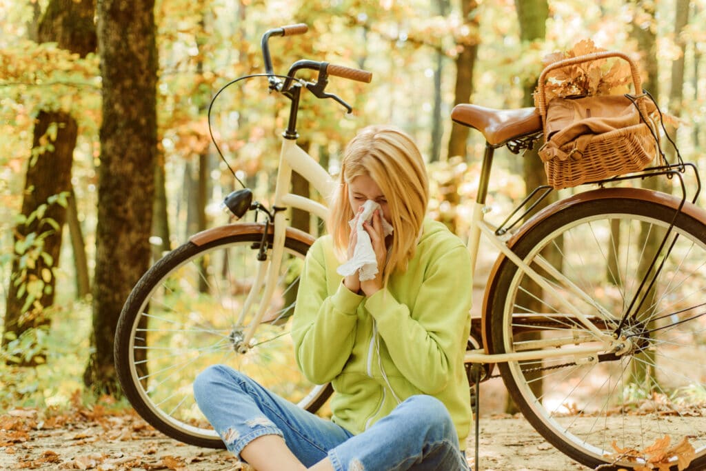 Woman outside next to bike blowing her nose due to seasonal fall allergies